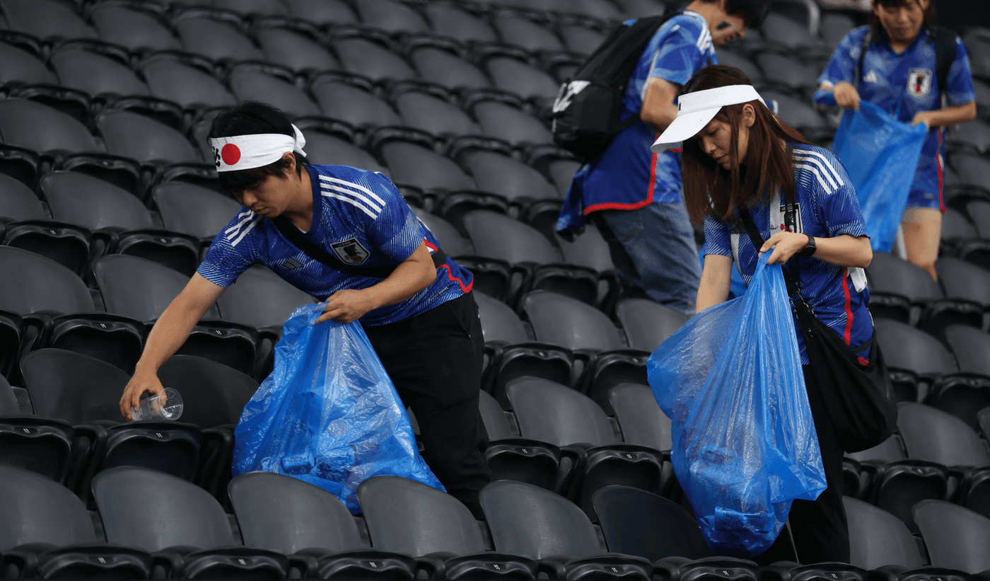 Japanese World Cup fans in blue jerseys collecting litter into blue plastic bags at Dallas Stadium after a 2-2 draw with the Netherlands on June 14 2026