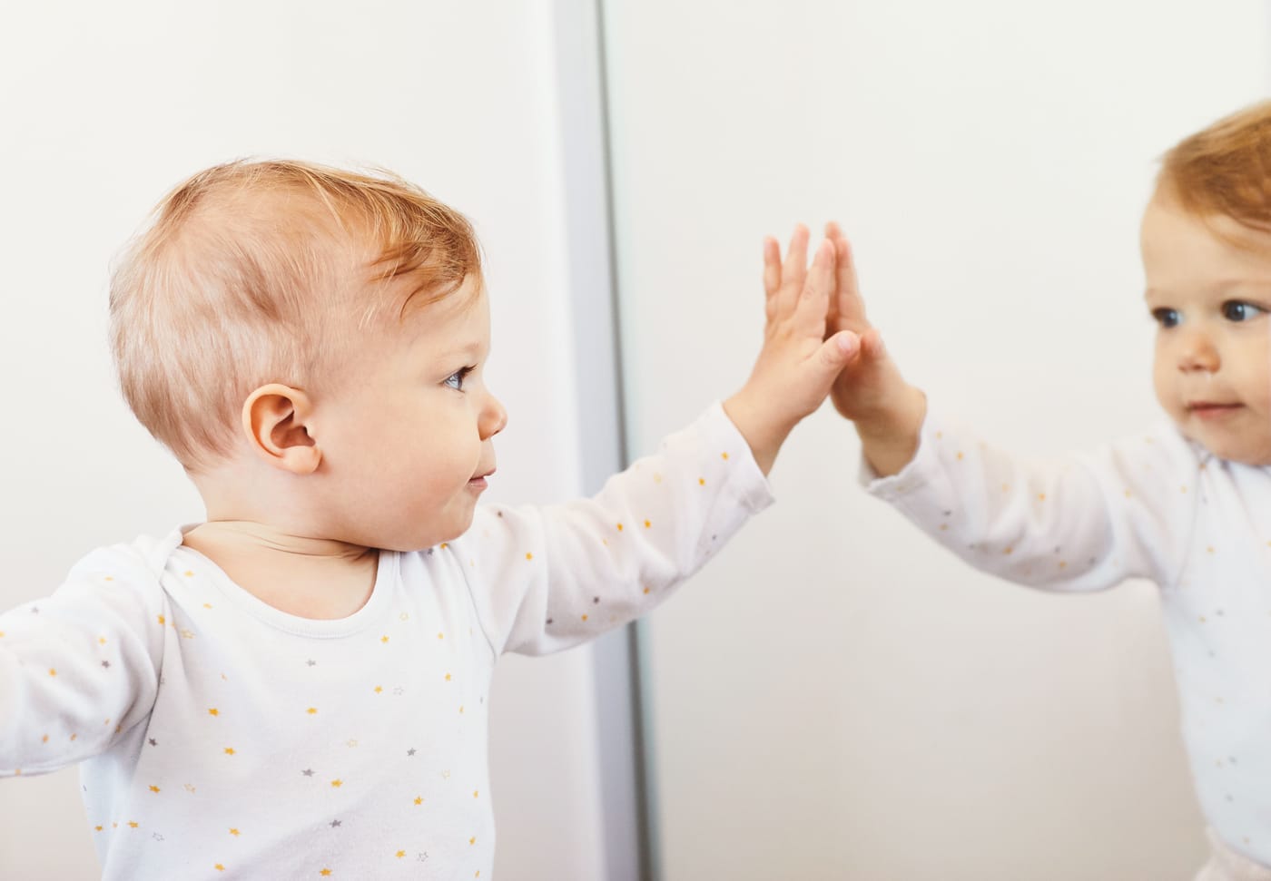 Four-month-old baby looking at its own reflection in a mirror representing new University of Birmingham research published in Developmental Science showing mirror play changes sensorimotor brain activity